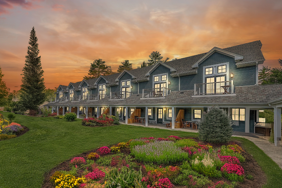 A row of cozy houses with balconies, set against a sunset sky. Beautifully landscaped gardens and lush greenery surround the scene.