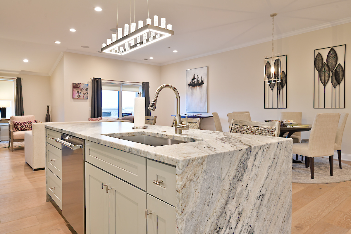 A modern kitchen and dining area with a marble island, stainless steel appliances, dining table, chairs, and contemporary artwork on the walls.