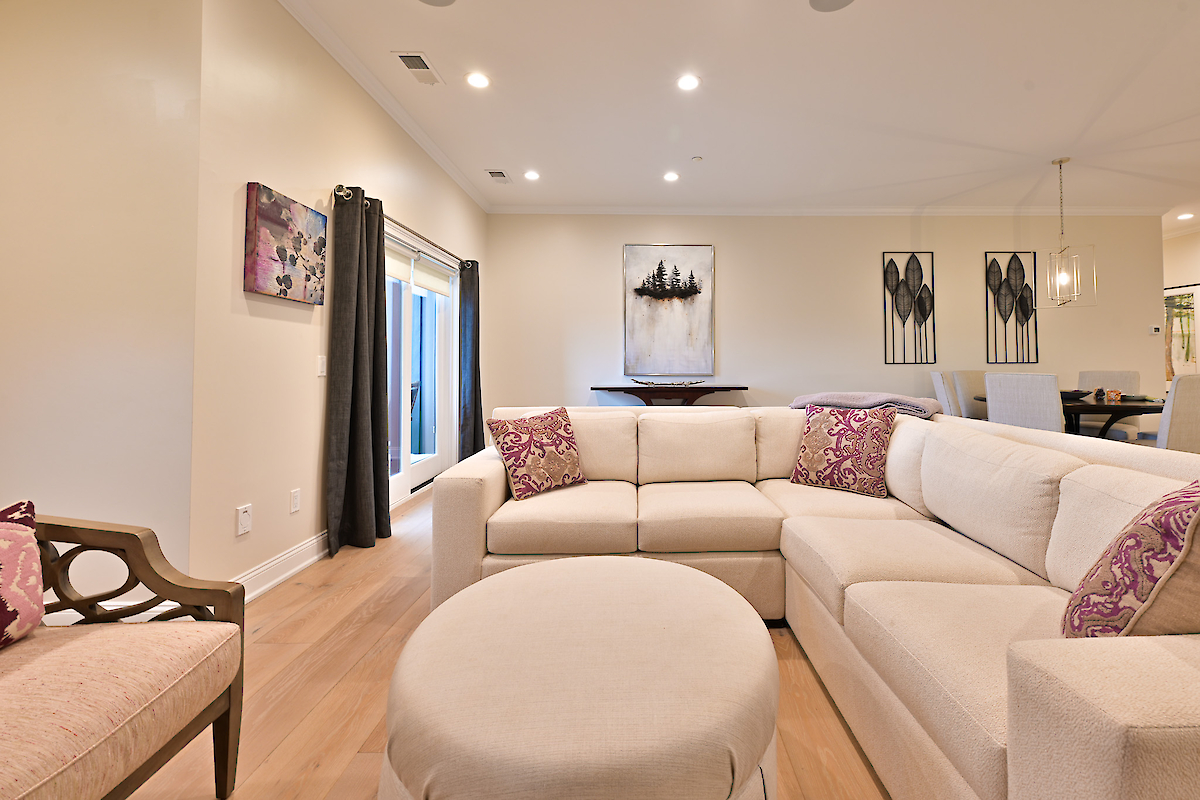 A cozy living room with a beige sectional sofa, an ottoman, wall art, and soft lighting, creating a warm and inviting atmosphere.
