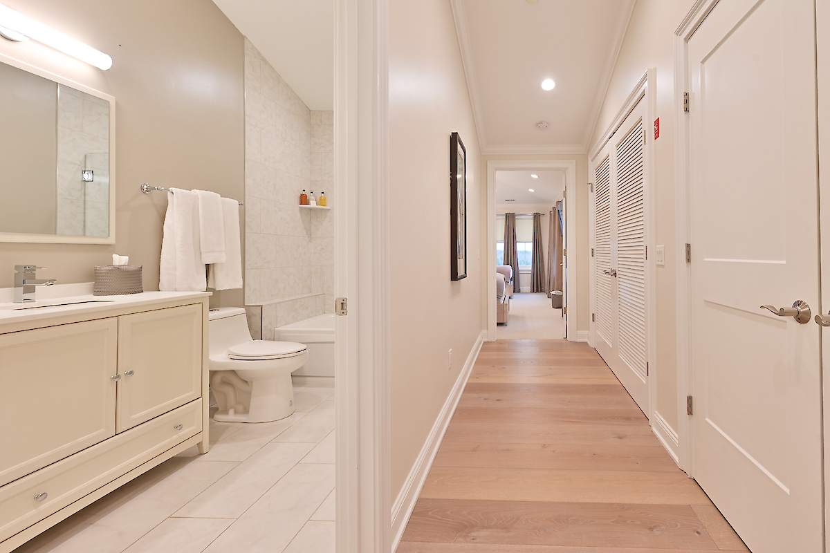 A hallway features light hardwood floors, a bathroom with a vanity and toilet visible on the left, and leads to what appears to be a bedroom at the end.