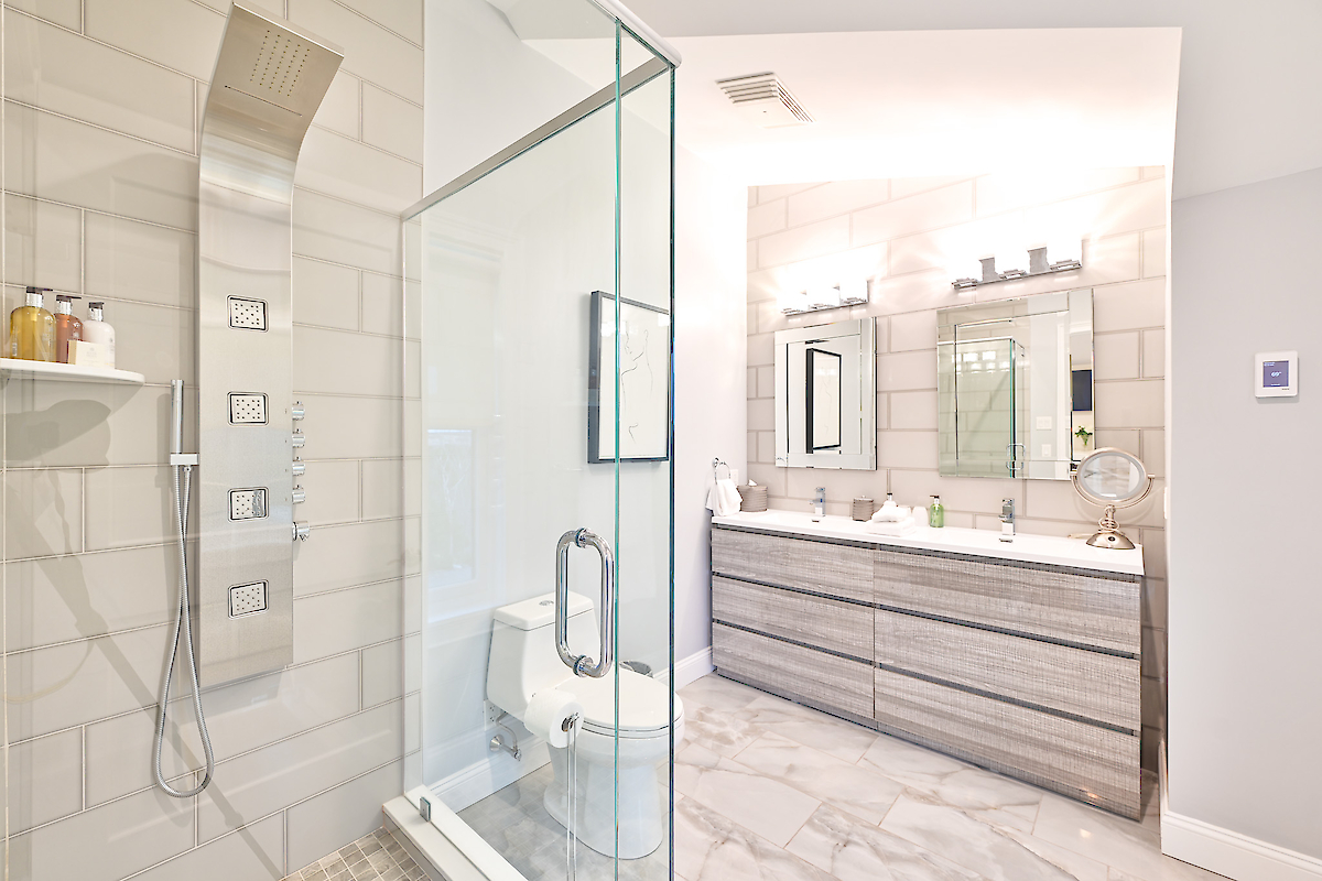 Modern bathroom with a glass shower enclosure, dual sinks, large mirror, and light fixtures above. Neutral tones and sleek design elements.