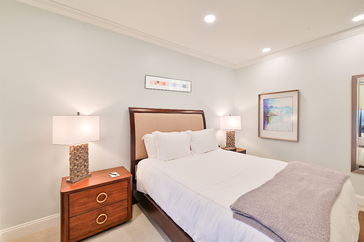 A neatly arranged bedroom with a double bed, two bedside tables with lamps, and a blanket folded at the bed's foot. Art decorates the walls.