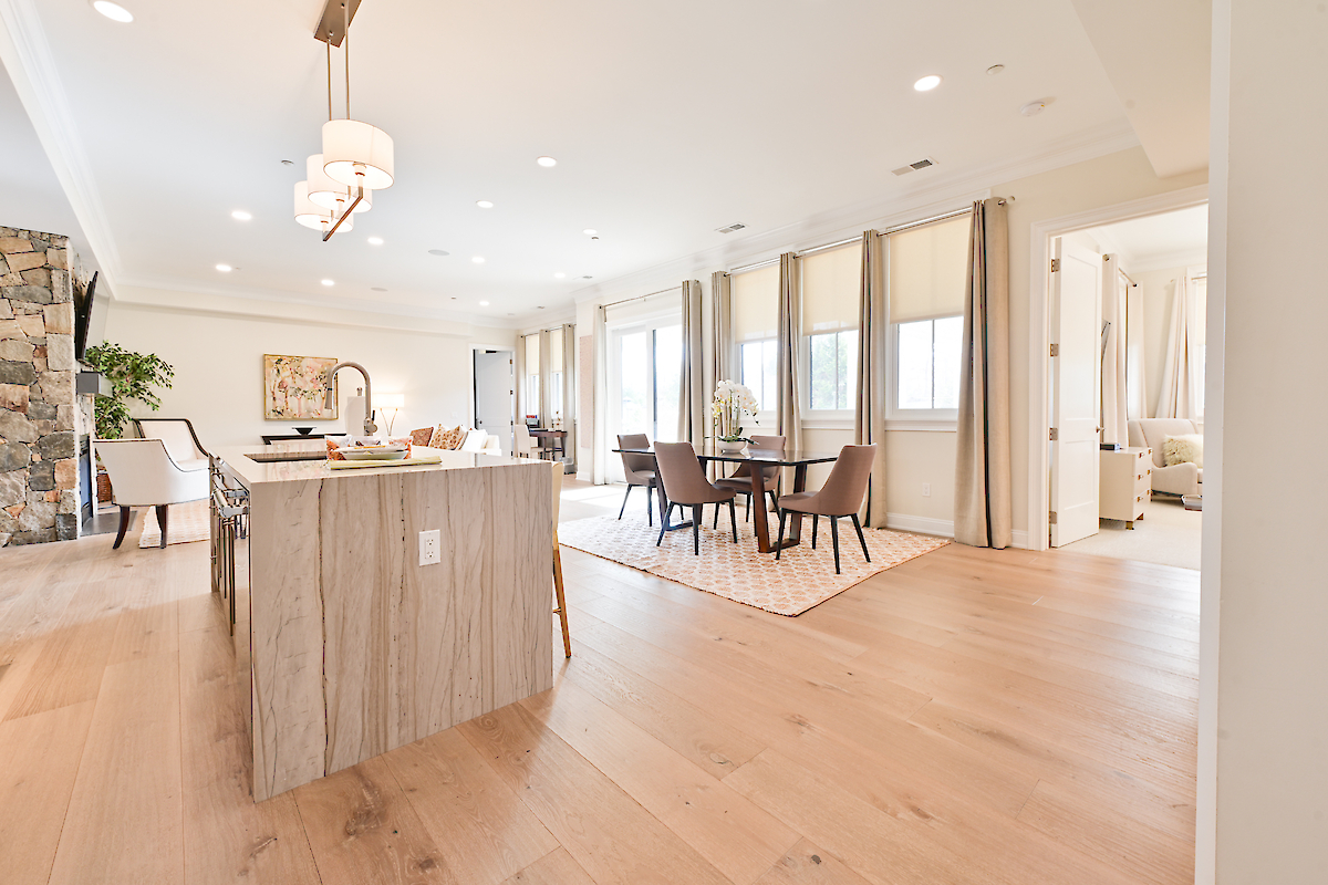 An open-concept living space features a kitchen island, dining area, large windows with curtains, light hardwood flooring, and modern decor.