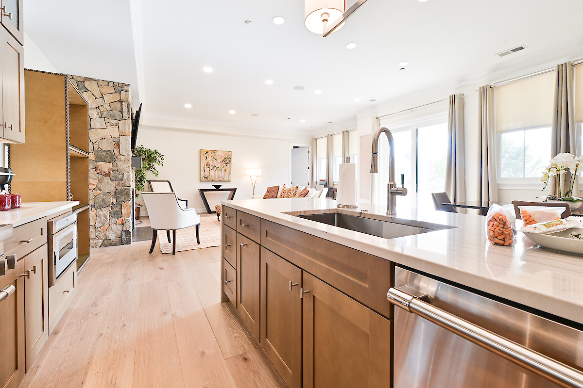A modern kitchen with wooden cabinets, a stone accent wall, and an open layout connecting to the dining area.