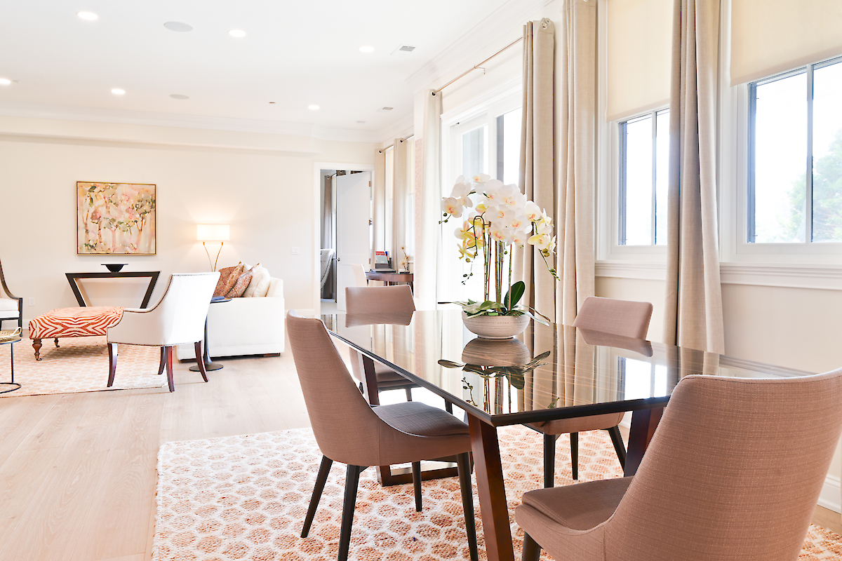 The image shows a modern dining and living area with a glass table, chairs, sofa, and windows with blinds.
