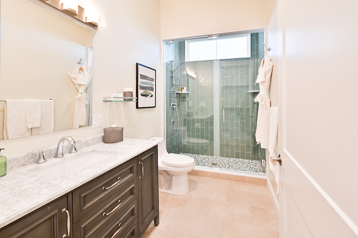 A modern bathroom with a marble countertop, sink, toilet, and glass-enclosed shower, featuring green tiles and wood cabinets for storage.