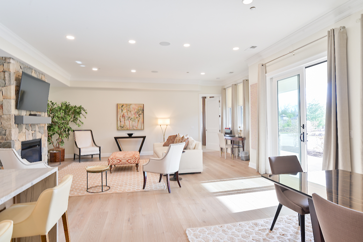 A spacious, brightly-lit living room with modern furniture, a TV, large windows, and a sliding glass door leading outside.