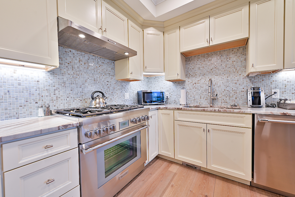 A modern kitchen with cream-colored cabinets, stainless steel appliances, a mosaic backsplash, a stove, microwave, and dishwasher are visible in the image.