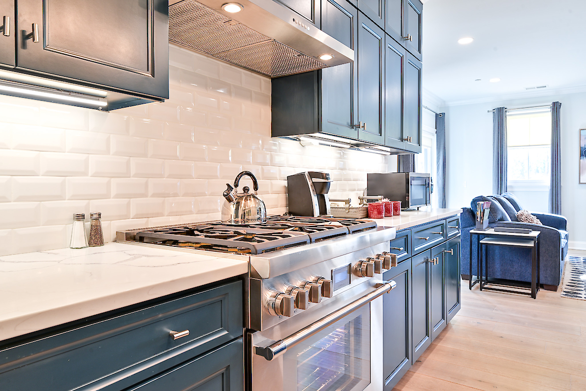 This image depicts a modern kitchen with navy blue cabinets, a stainless steel gas stove, a teapot, and a countertop with small appliances.