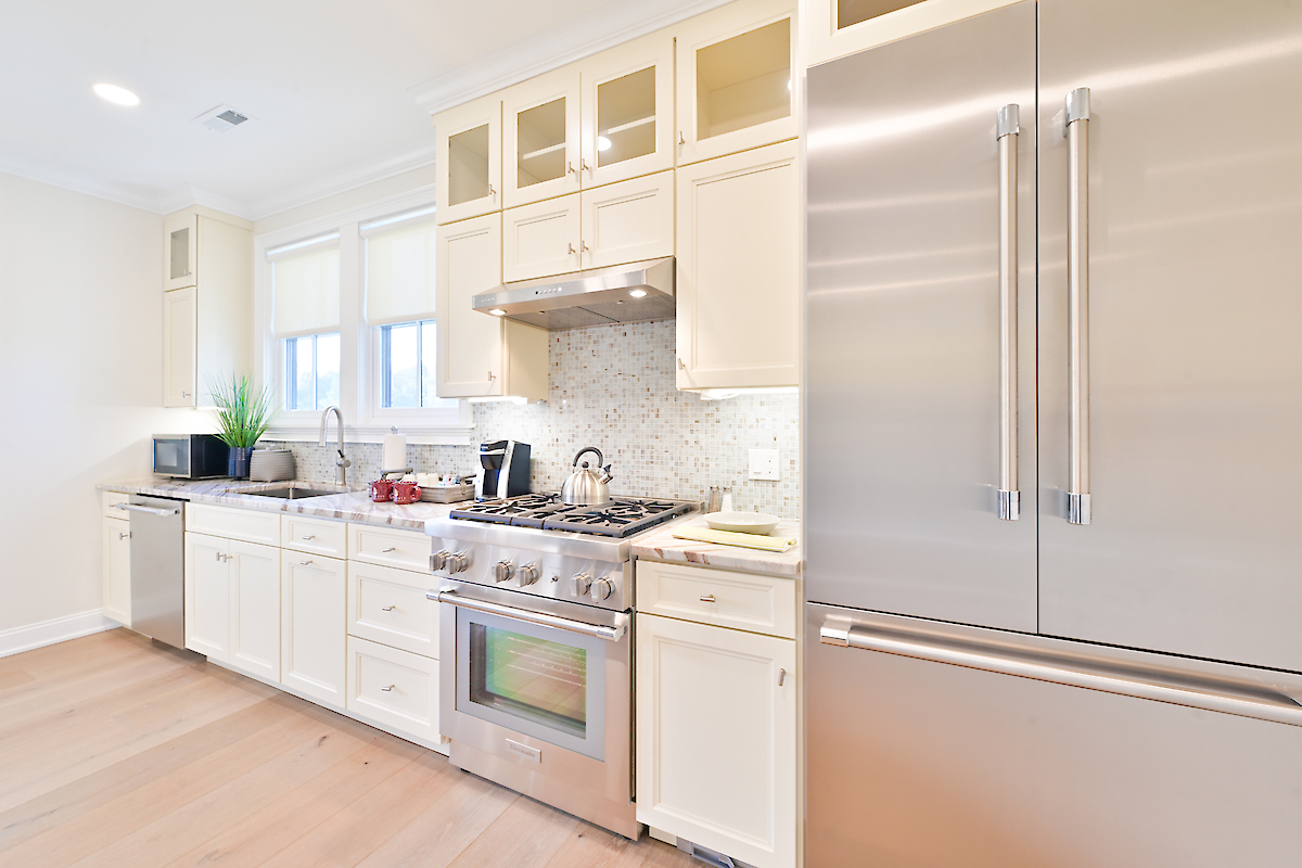 Modern kitchen with white cabinetry, stainless steel appliances, gas stove, double door fridge, potted plant, and wooden flooring.