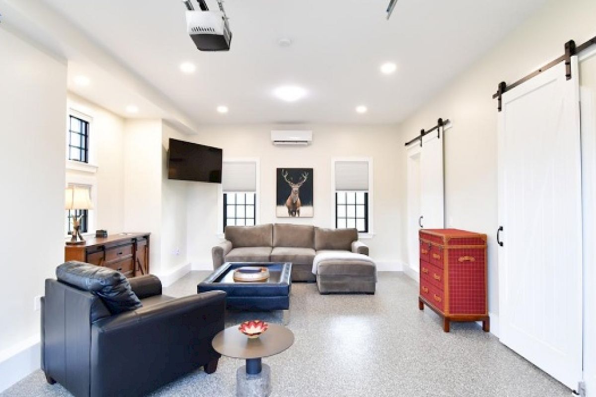 This image shows a modern living room with a sectional sofa, armchair, wall-mounted TV, barn doors, and a decorative deer painting.