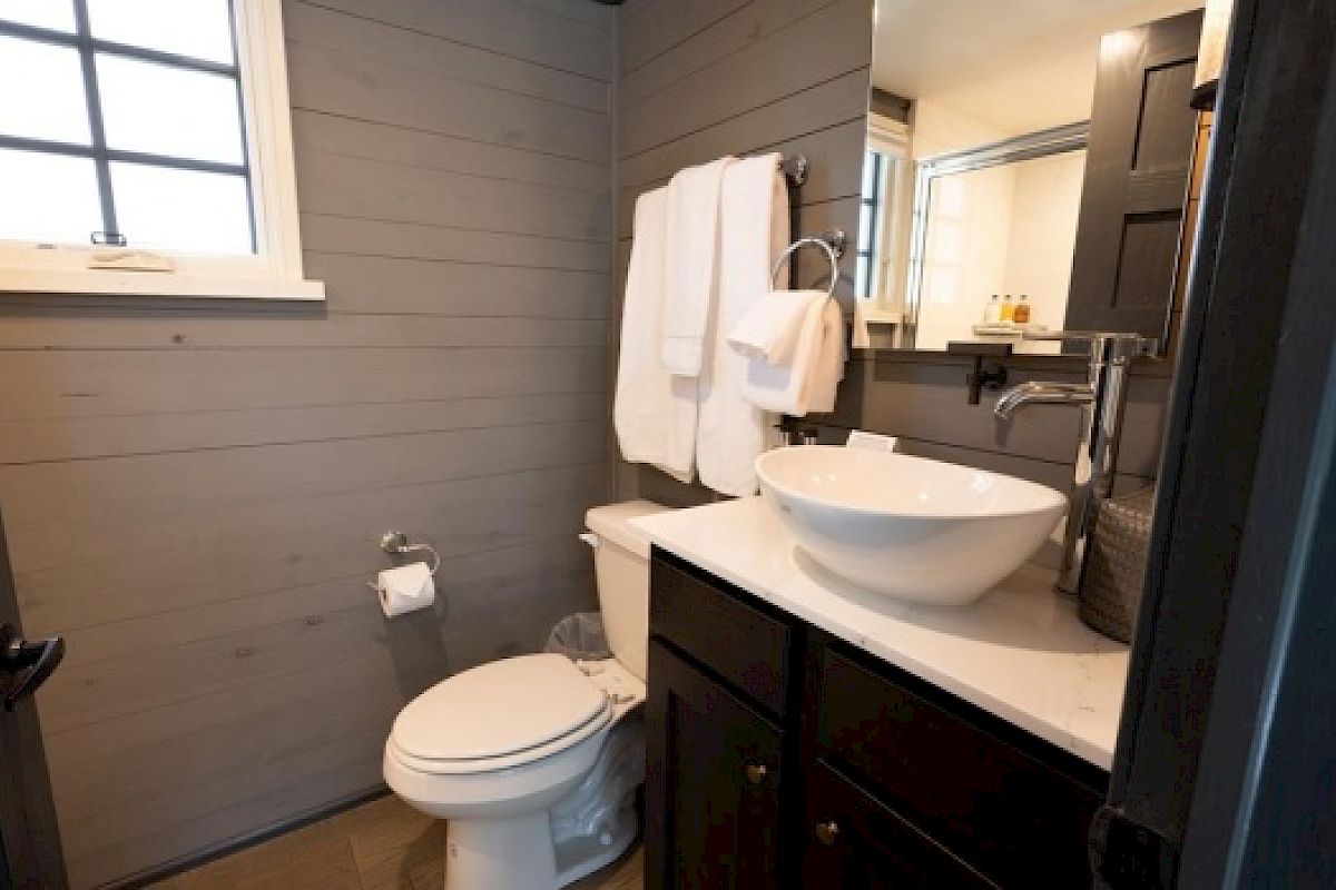 This image shows a small, modern bathroom with a vessel sink, a toilet, a towel rack with white towels, and a window with grid panes.