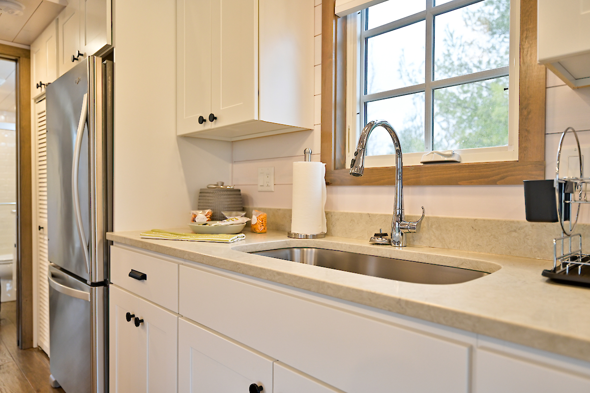 A modern kitchen featuring a stainless steel refrigerator, white cabinets, a sink with a chrome faucet, and a window with a wooden frame.