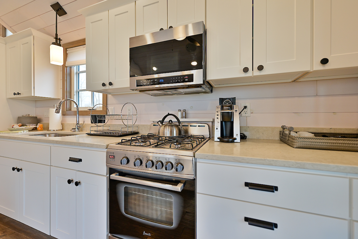 A modern kitchen with white cabinets, a stainless steel stove, microwave, sink with a faucet, and a coffee maker on the counter.