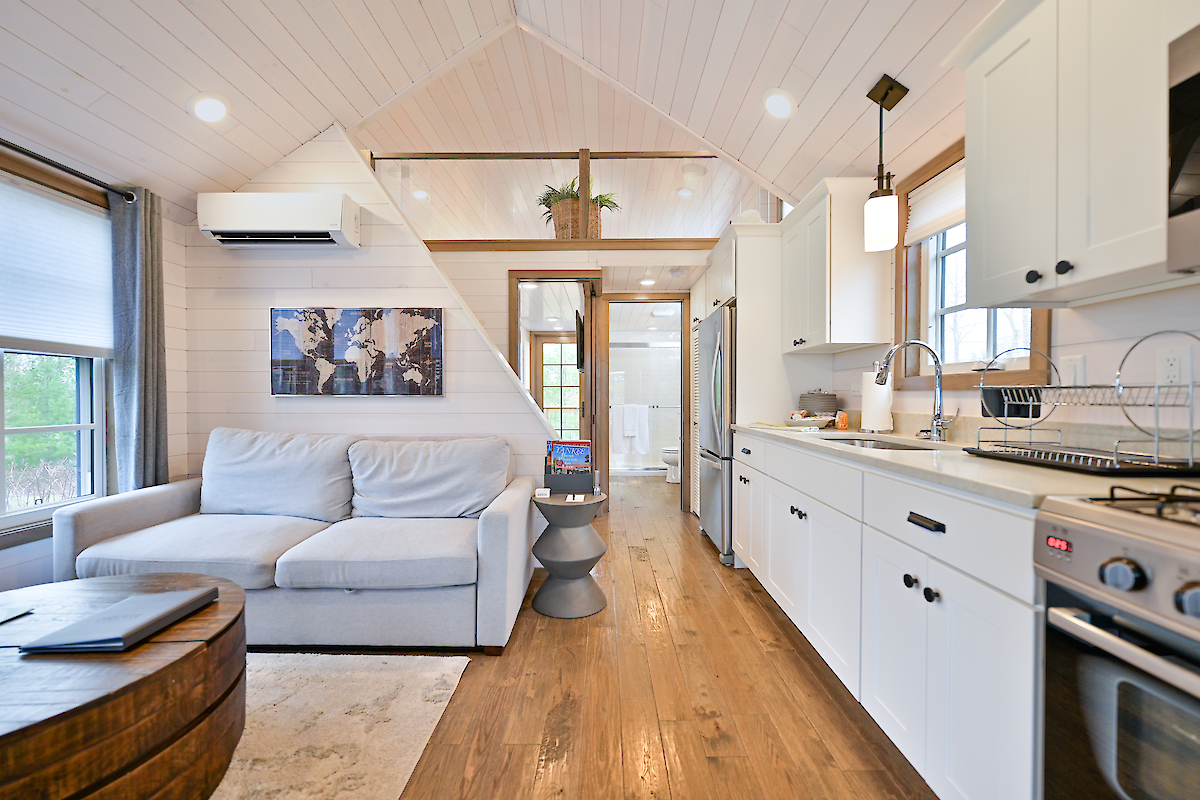 A cozy, modern tiny house interior with a living area on the left featuring a couch, and a compact kitchen on the right.