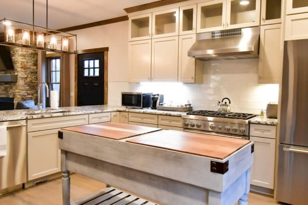 Modern kitchen with white cabinets, stainless steel appliances, a central island with a butcher block top, and a chandelier lighting fixture overhead.