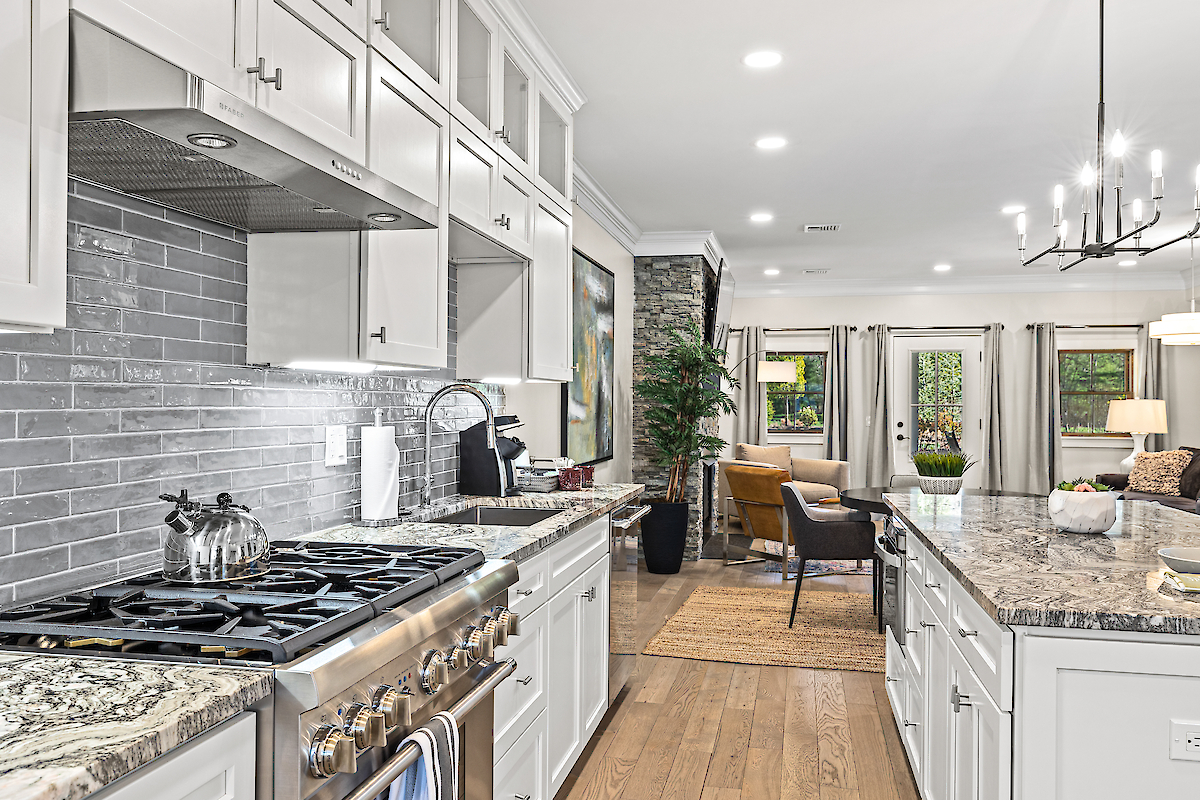 This image shows a well-lit, modern kitchen with granite countertops, white cabinetry, and stainless steel appliances, opening into a cozy living area.