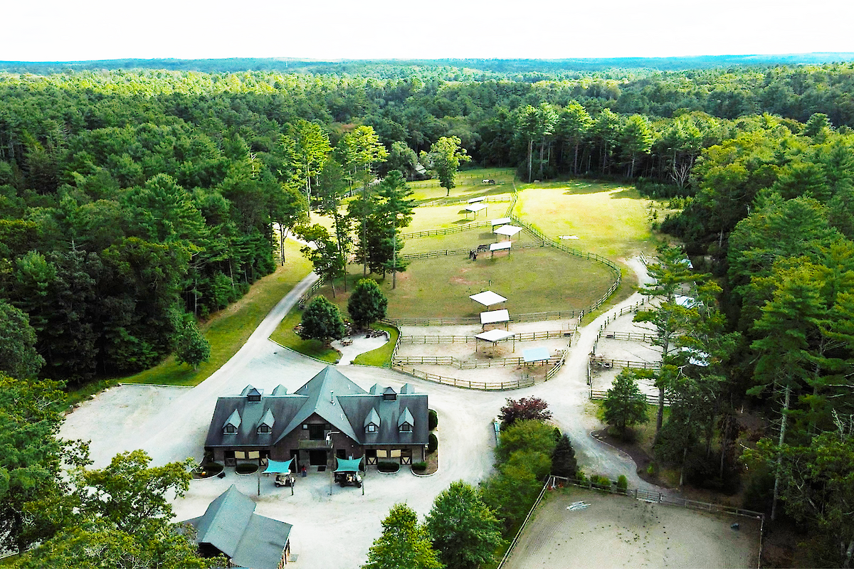 A large, wooded property with a central building, surrounding pastures, and dirt paths, possibly a ranch or retreat, surrounded by dense forest.
