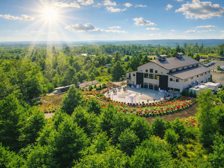 A scenic view of a large building surrounded by lush greenery and gardens under a sunny, blue sky with scattered clouds.