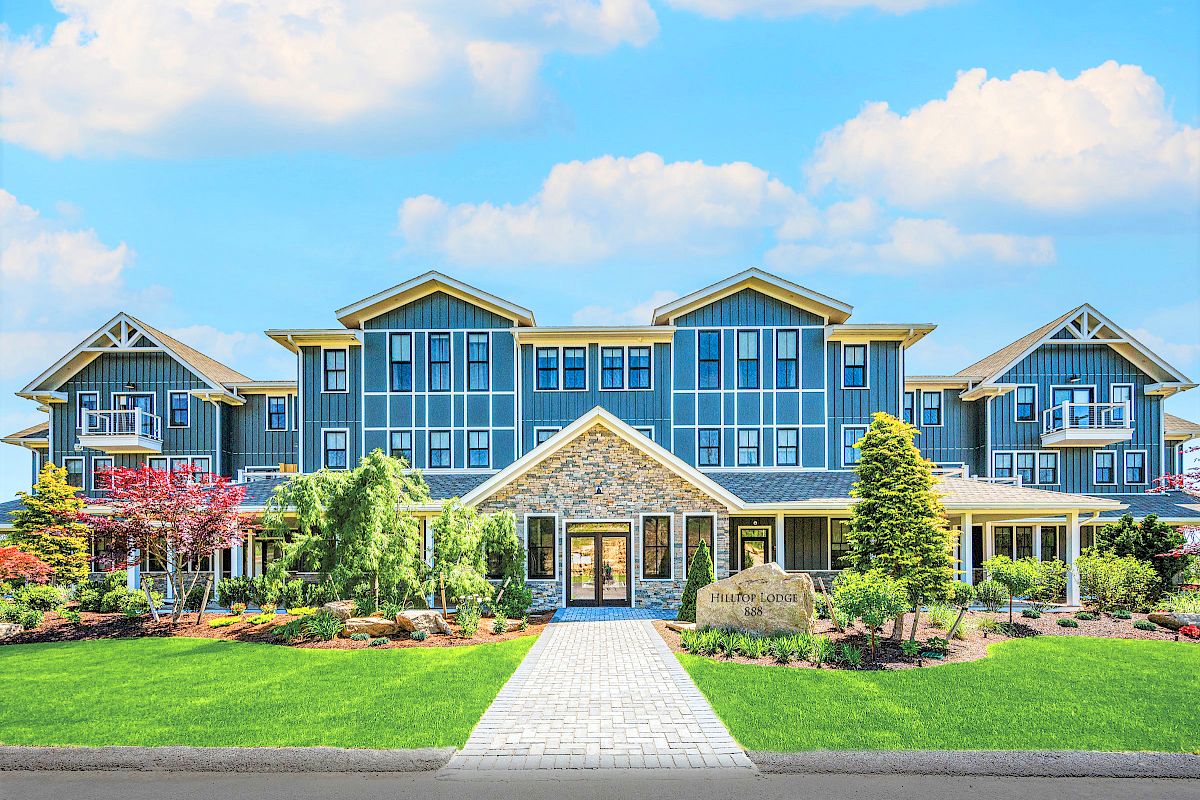 A large, modern, blue building with white trim, surrounded by well-kept gardens and greenery under a partly cloudy sky.