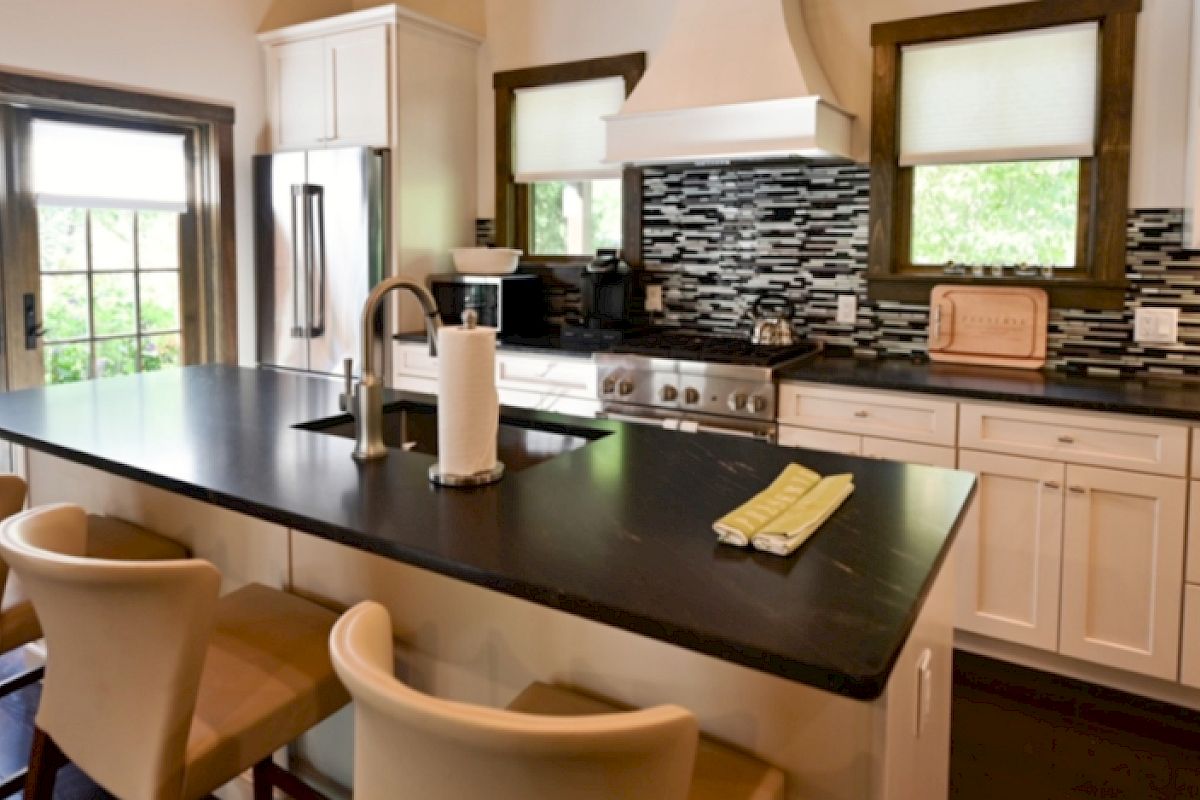 A modern kitchen with a central island, black countertops, white cabinets, stainless steel appliances, and bar stools.