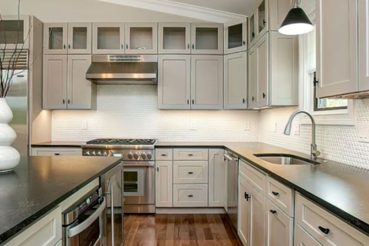 Modern kitchen with stainless steel appliances, white cabinets, dark countertops, a central island, and wooden floors.