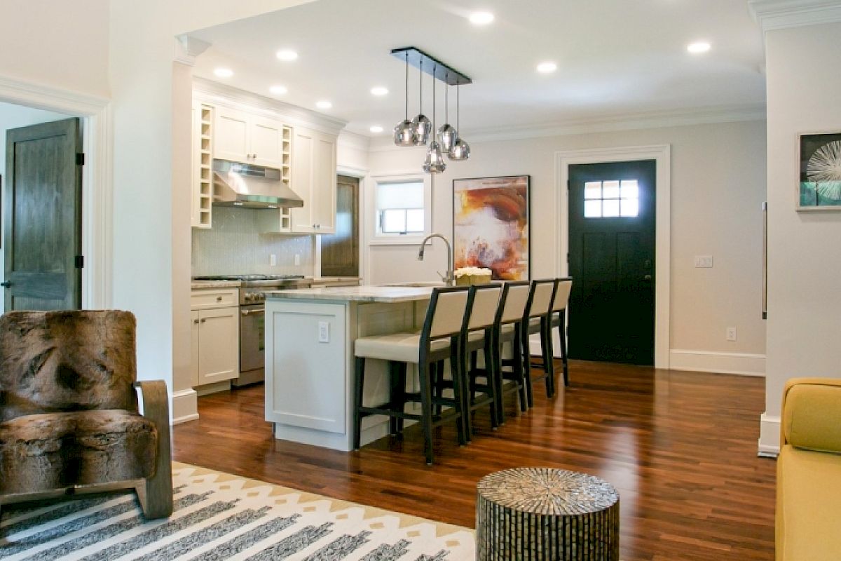 A modern open-concept living space with a kitchen, island seating, wooden floors, stylish furnishings, and contemporary lighting.