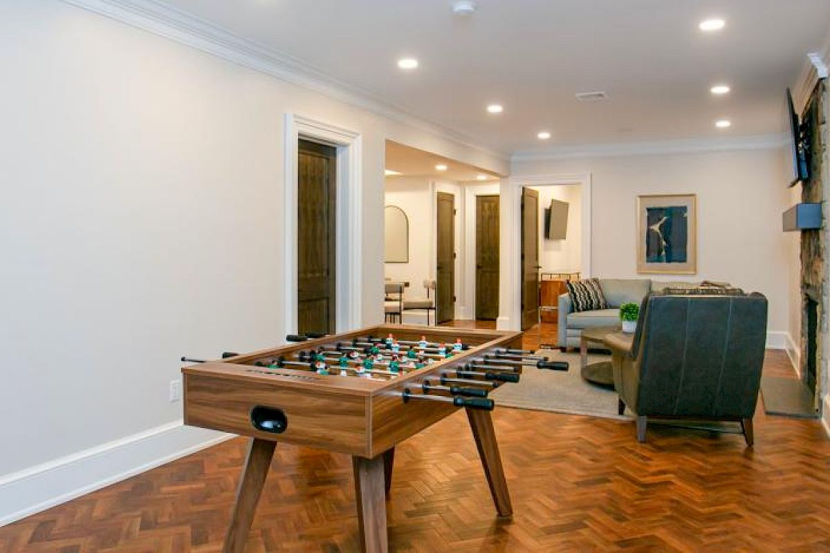 A game room with a foosball table, a seating area with a TV, and artworks on the walls; wooden flooring enhances the cozy atmosphere.
