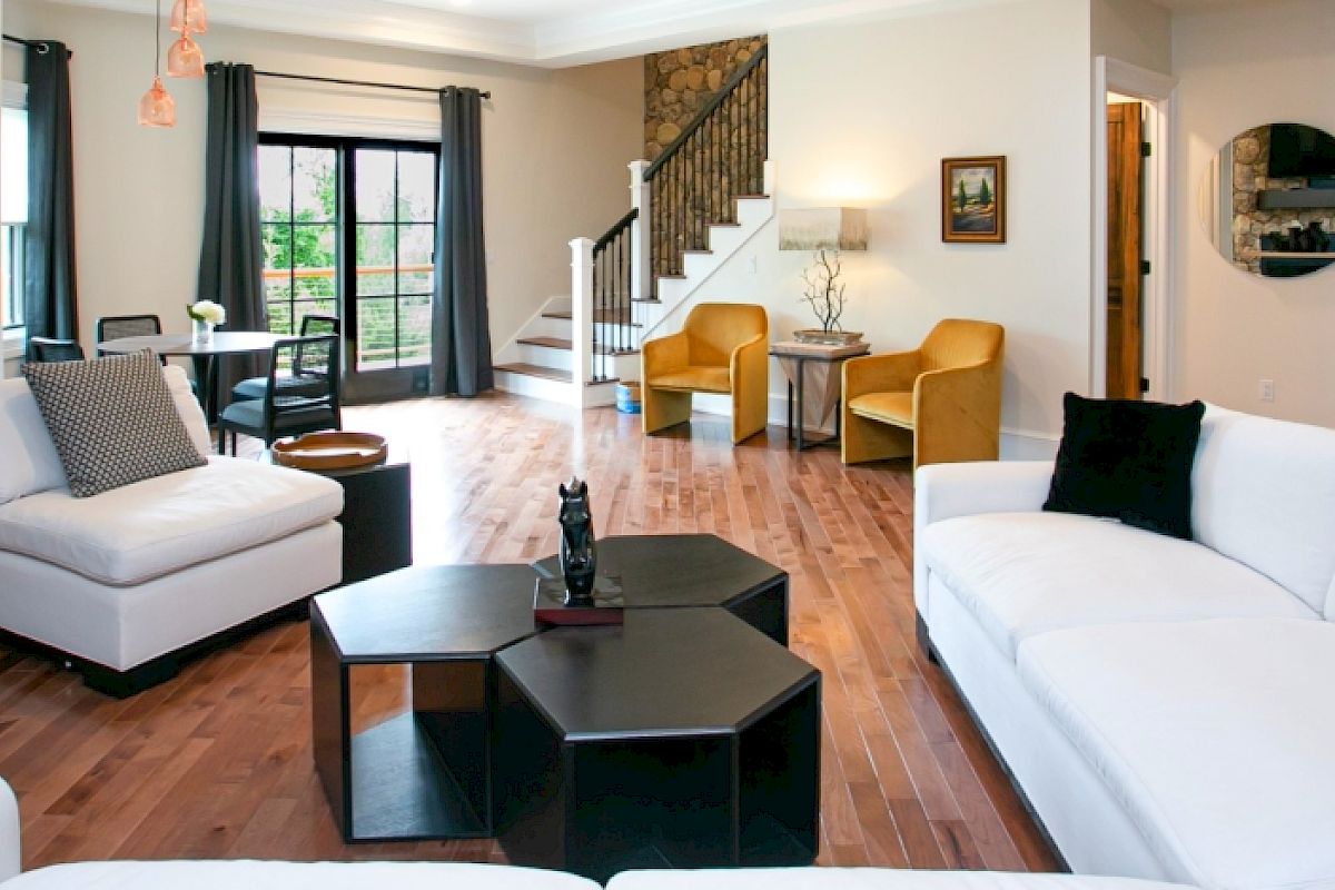 A modern living room with white sofas, a stone fireplace, hexagonal coffee tables, and yellow chairs near a staircase.