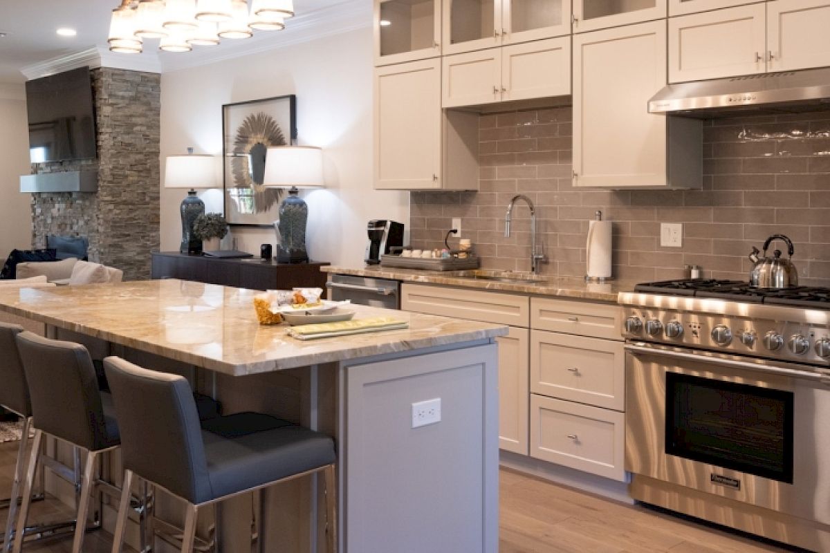A modern kitchen with an island, four stools, stainless steel appliances, beige cabinetry, and an adjacent dining area, ending the sentence.