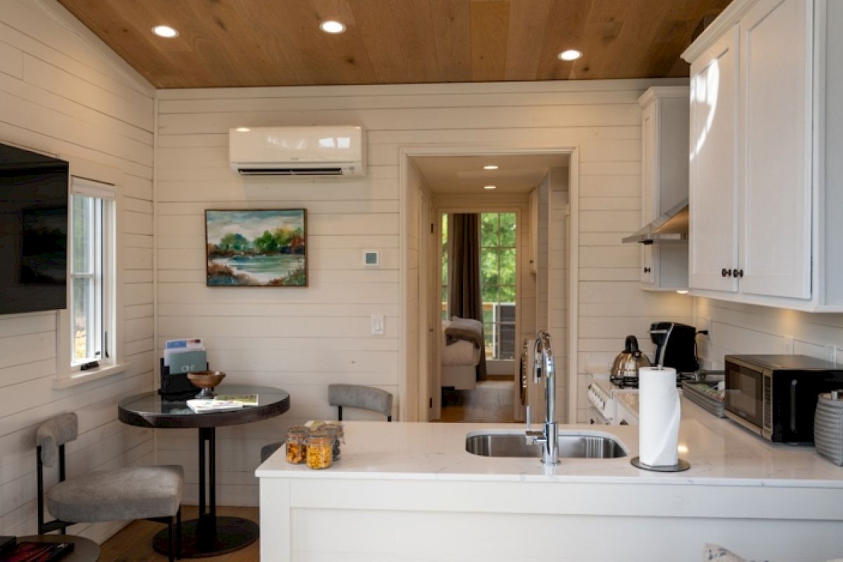 A cozy, modern kitchen and dining area in a small living space, featuring a TV, round table, sink, cabinets, and an air conditioner.