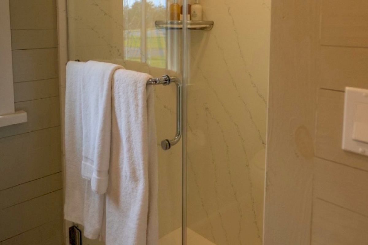 The image shows a bathroom with a glass shower door, a white towel hanging, a window, and light switches on a wooden wall ending the sentence.
