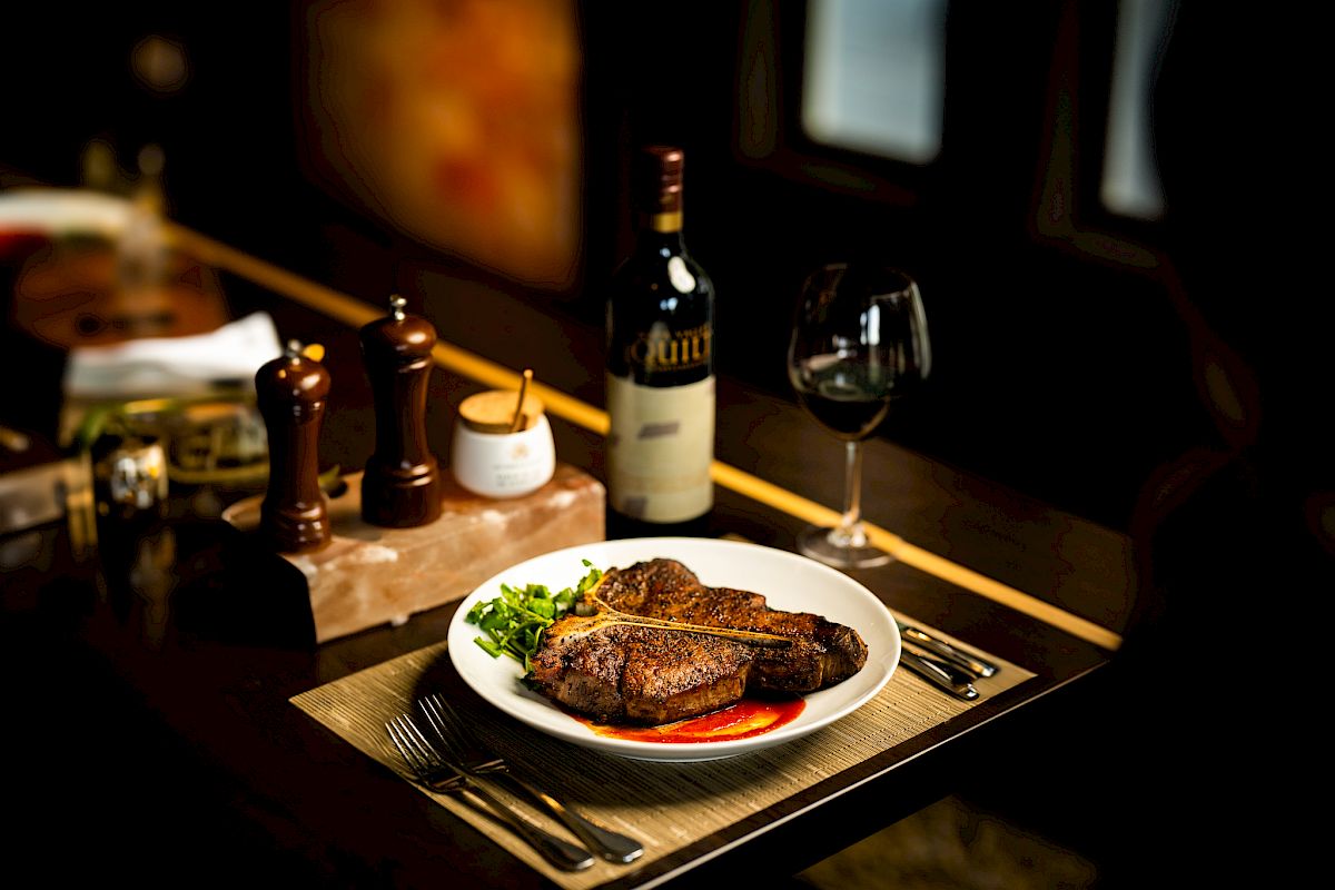 A plate of perfectly cooked steak with green vegetables, paired with a glass of red wine and a bottle, set on a table at Double Barrel Steak at The Preserve.