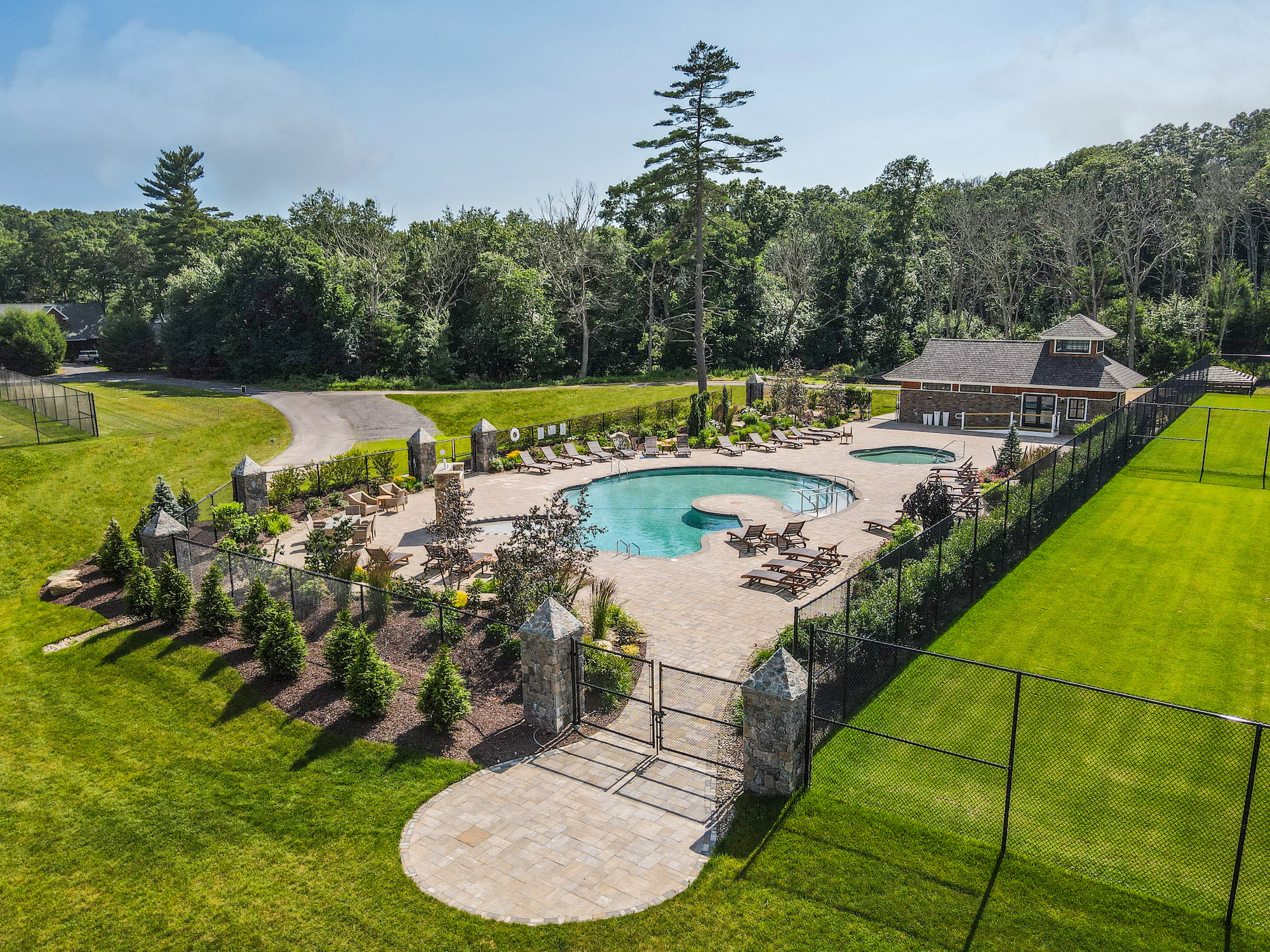 The image depicts an outdoor recreational area with a large swimming pool surrounded by lounge chairs, landscaping, and a building, nestled in greenery.