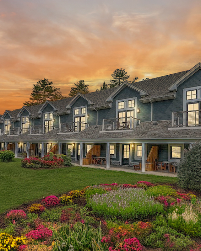 A picturesque building with a row of units, lush gardens, and a vibrant sunset sky in the background, creating a serene and inviting scene.