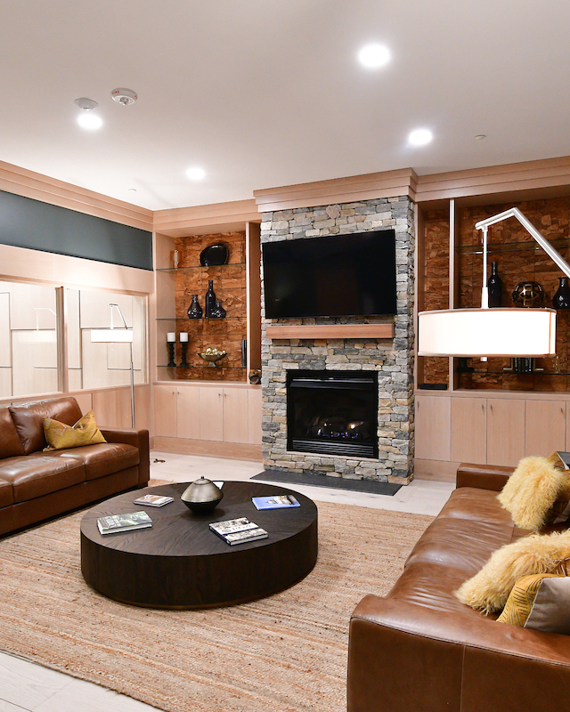 A modern living room with leather sofas, a fireplace, TV, and large artwork on the wall, featuring a cozy, well-lit ambiance.