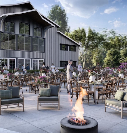 An outdoor event space with many chairs and tables, a fire pit, and a large building in the background surrounded by trees and flowers.