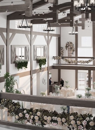 A beautifully decorated two-story venue with wooden beams, chandeliers, flowers, and plants, ideal for weddings or events.