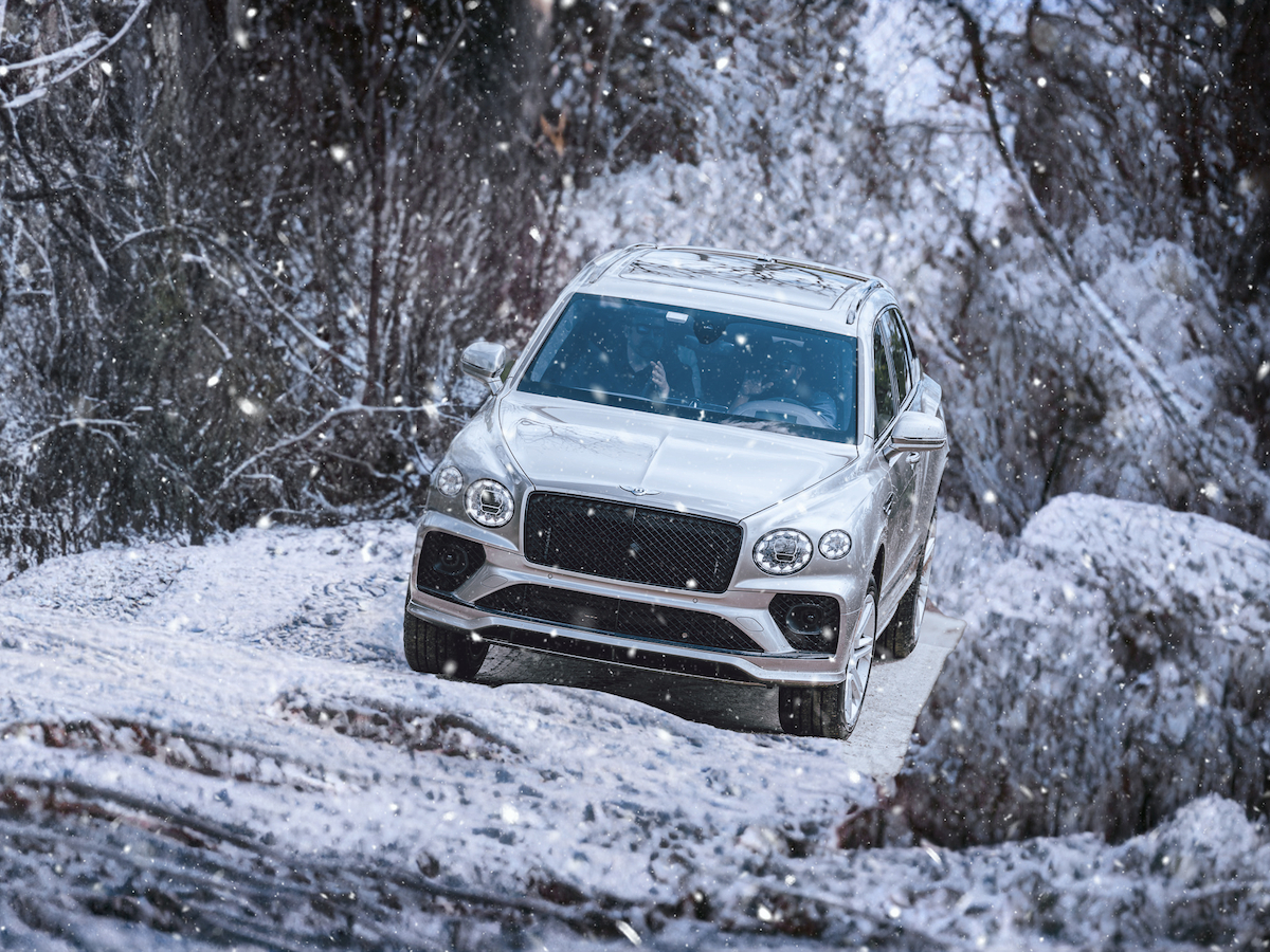 An SUV is driving through a snowy forest, surrounded by snow-covered trees.