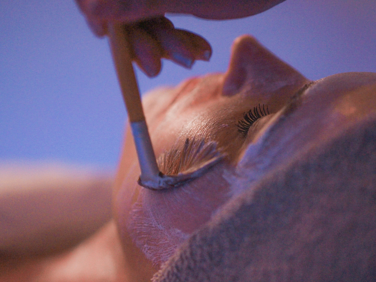 A person is receiving a facial treatment with a brush applying a mask or cream while they relax, likely in a spa setting.