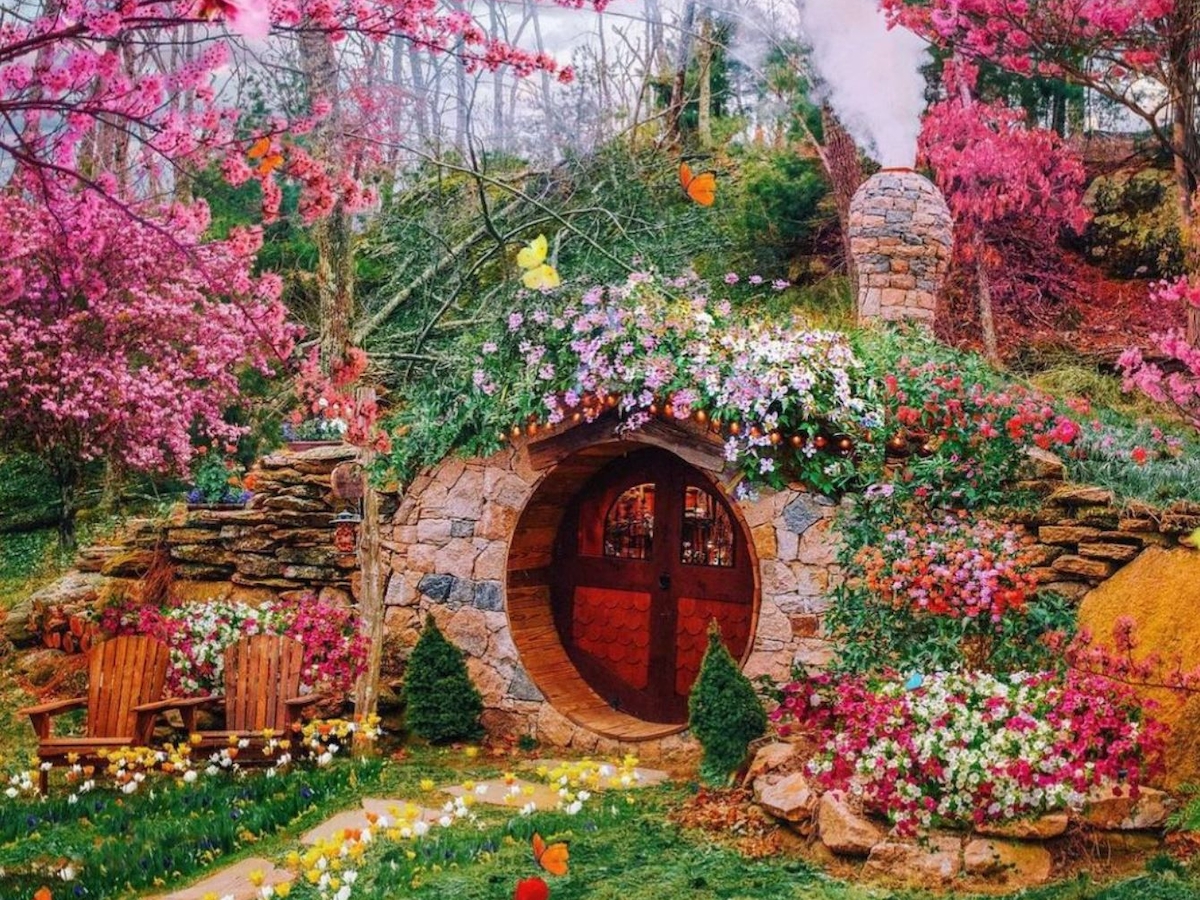 A hobbit-like house nestled in a vibrant garden with tulips, cherry blossoms, and lush greenery, creating a whimsical, fairytale atmosphere.