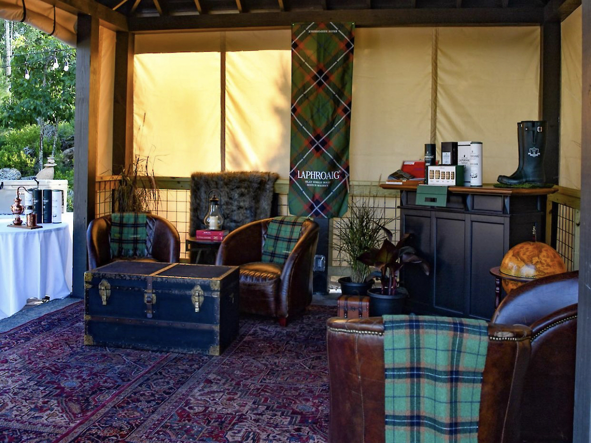 A cozy room with a vaulted ceiling features armchairs, a chest, plaid accents, a rug, and a chandelier, creating a rustic ambiance.
