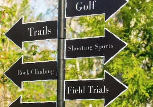 A signpost with arrows points to activities: Golf, Trails, Shooting Sports, Rock Climbing, Field Trials, Zip Line, and Fishing.