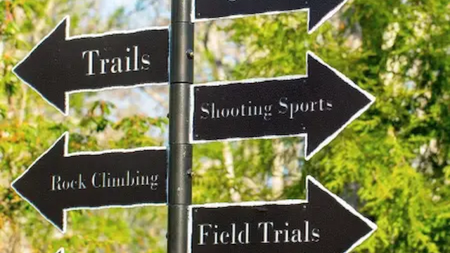 A signpost with arrows points to activities: Golf, Trails, Shooting Sports, Rock Climbing, Field Trials, Zip Line, and Fishing.