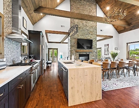 A modern kitchen and dining area with wooden floors, stone accents, high ceilings, and natural light.