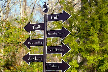 The image shows a signpost with arrows pointing to Golf, Trails, Shooting Sports, Rock Climbing, Field Trials, Zip Line, and Fishing.