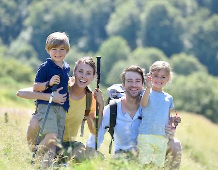 A family of four is smiling outdoors in a grassy field, with trees in the background, suggesting a fun day out in nature.