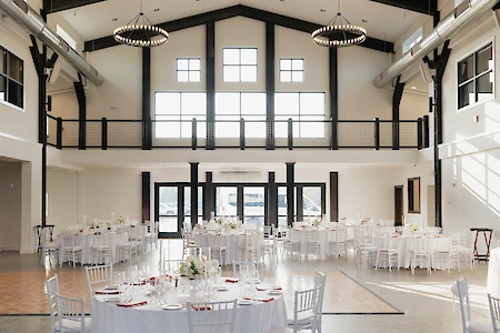 A large, elegant event hall set for a function with round tables, white chairs, and floral centerpieces under high ceilings and chandeliers.