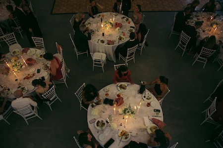 An overhead view of a formal event with guests seated around candlelit tables with food and drinks.