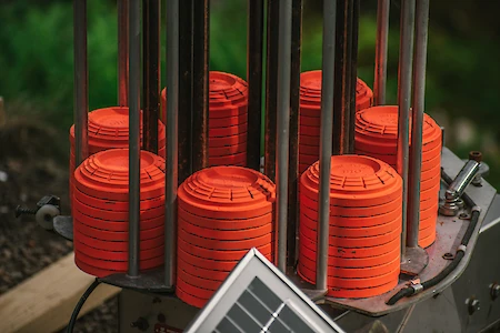 The image shows stacks of orange clay targets loaded onto a trap shooting machine, with a solar panel visible in the foreground.